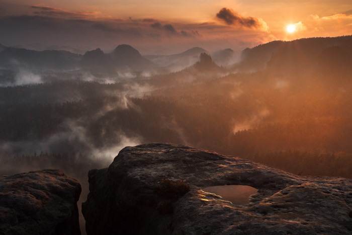 Misty mountain range at sunrise with rock foreground