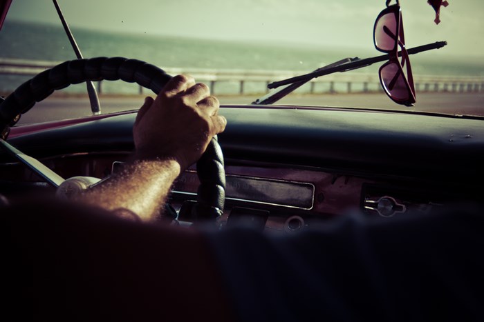 Man driving a vintage car with sunglasses hanging