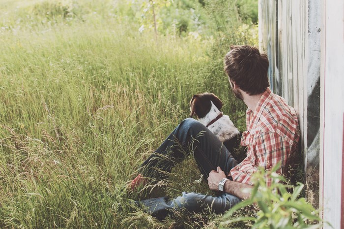 Man and dog sitting by a concrete wall in tall grass