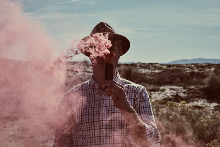 Man in hat with pink smoke grenade in desert
