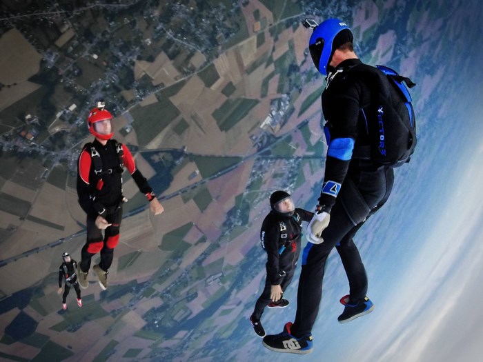 Four skydivers freefall over a rural landscape
