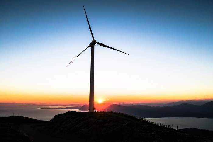 Wind turbine silhouetted against a sunrise over mountains and water