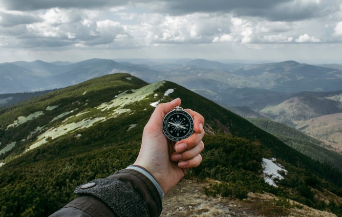 Hand holding a compass in a mountain range