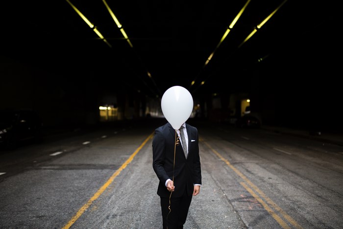 Man in Suit Holding White Balloon on Dark Road
