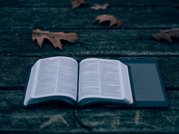 Open Bible and Tablet on Wooden Table with Leaves