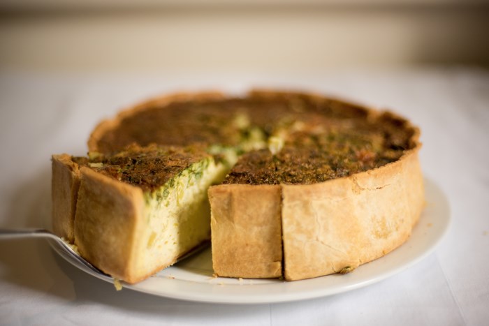 A slice of quiche is being served from a whole quiche on a plate.