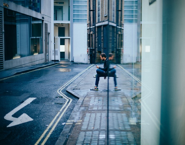 Man sitting on pavement with phone in city street