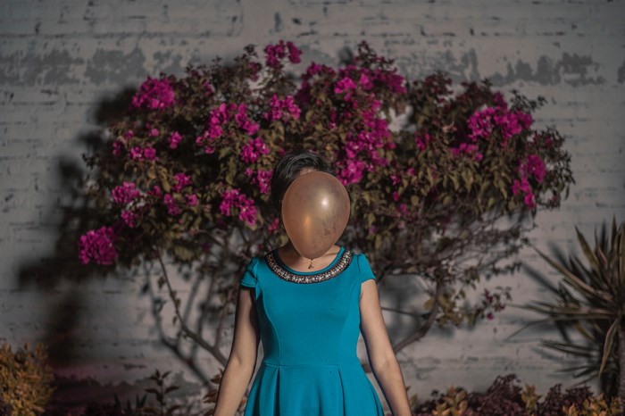 Woman in blue dress with balloon covering face