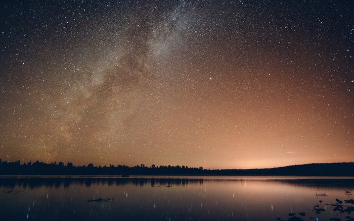 Starry night sky over a calm lake and forest