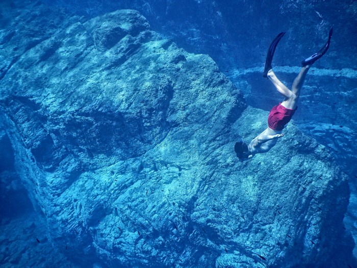 Freediver in red shorts swims near a large rock formation