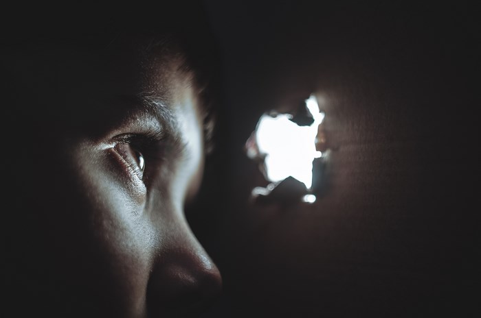 A person peeks through a hole in the dark