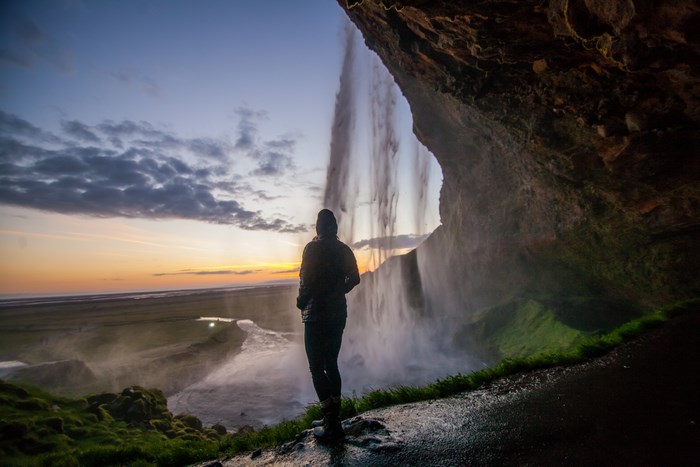 Person standing under a waterfall in Iceland at sunset