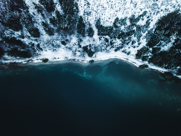 Aerial view of a snow-covered forest meeting a dark lake