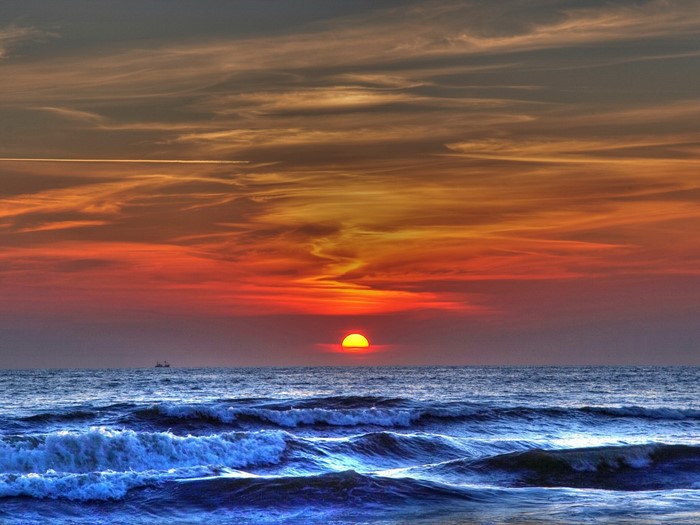 Sunset over the ocean with waves and ships