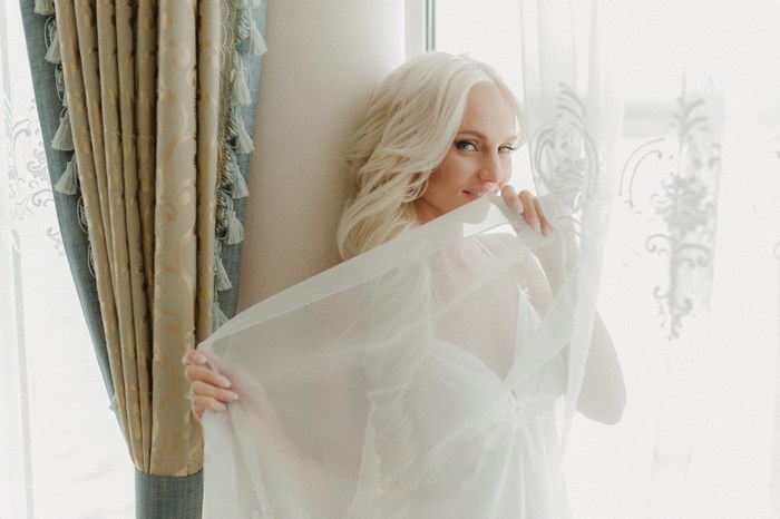 Woman in white lingerie behind sheer fabric near curtains