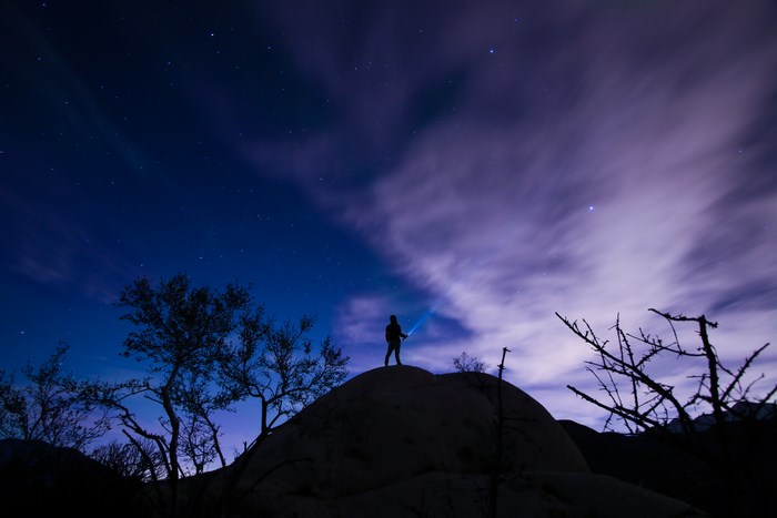 Person with flashlight on hill under starry sky