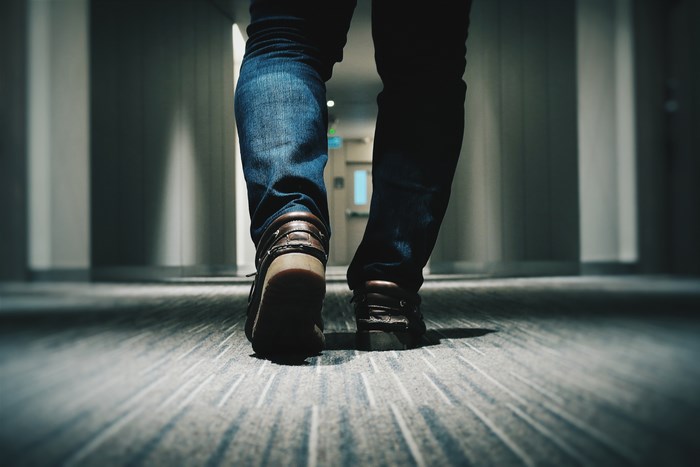 Man in jeans and loafers walking down a carpeted hallway