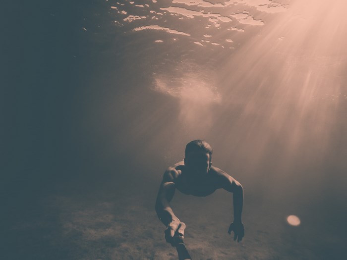 Man holding selfie stick underwater with sunrays