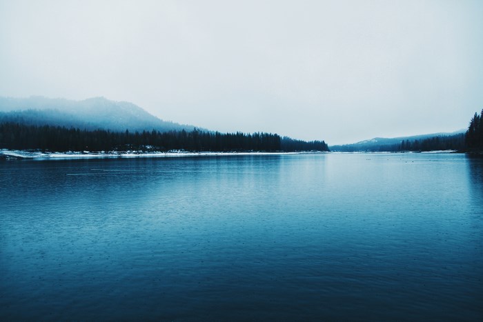 Blue lake with forest and mountains on a cloudy day
