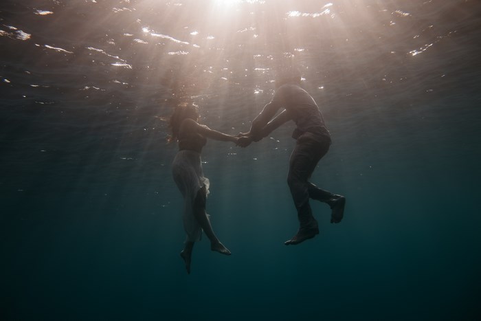 Couple holding hands underwater with sun rays