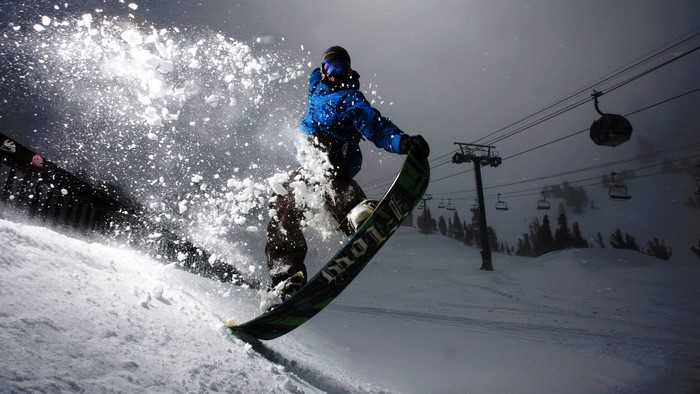 Snowboarder performing a trick with snow spray and ski lift