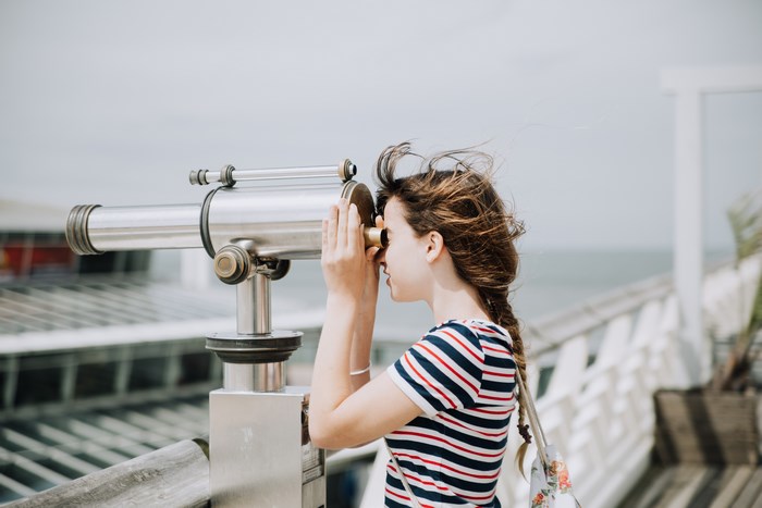 Woman looking through a telescope on a pier