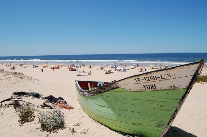 Green boat named Yuri on a crowded beach