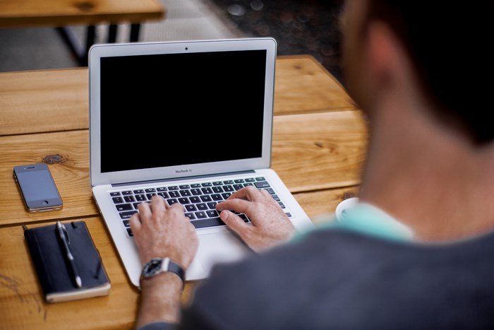 Man typing on a MacBook Air laptop at a wooden table