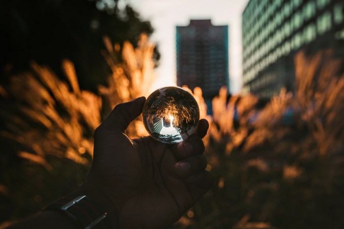 Hand holding glass ball reflecting sunset in urban setting