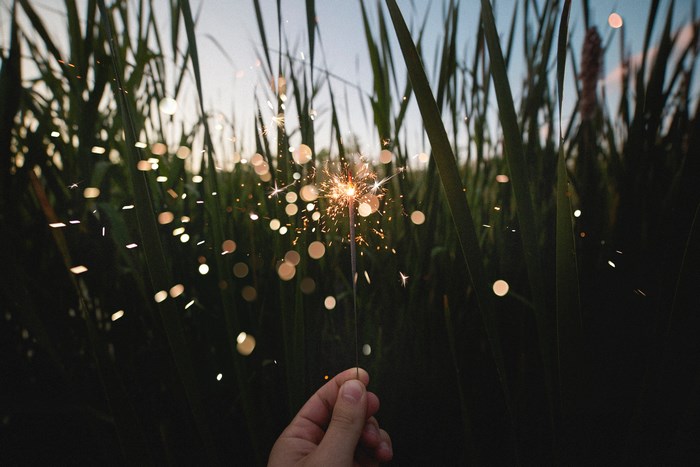Hand holding a sparkler in tall grass