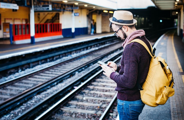 Man with backpack using smartphone at train station