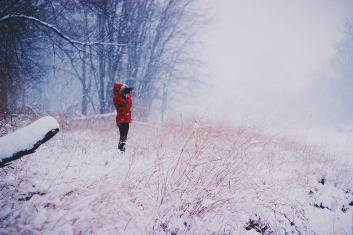 Woman in red parka taking photo in snowy landscape