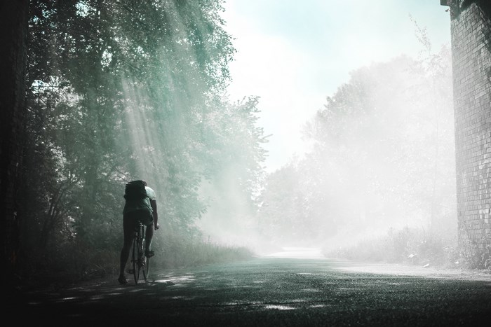 Cyclist with backpack riding on a misty road with sunrays