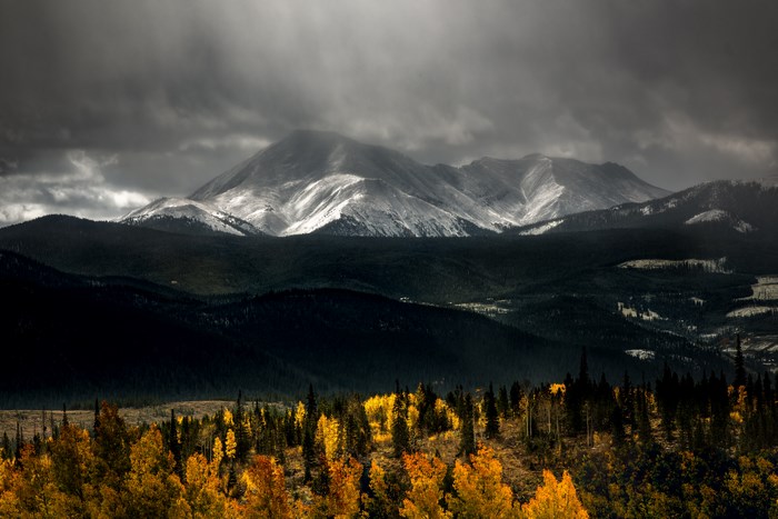 Snow-capped mountains under stormy clouds with autumn trees