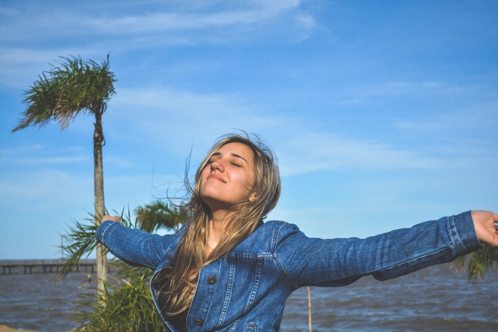 Woman in denim jacket with arms outstretched by the water