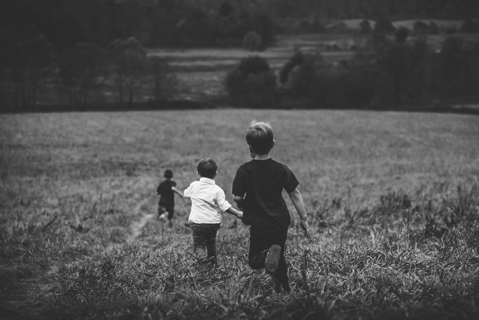 Three boys running through a grassy field