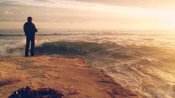 Man fishing on a sandy shore at sunset