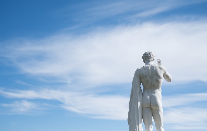 Marble sculpture of a man from behind against a blue sky