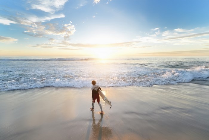 Boy Walking on Beach Holding Surfboard at Sunrise
