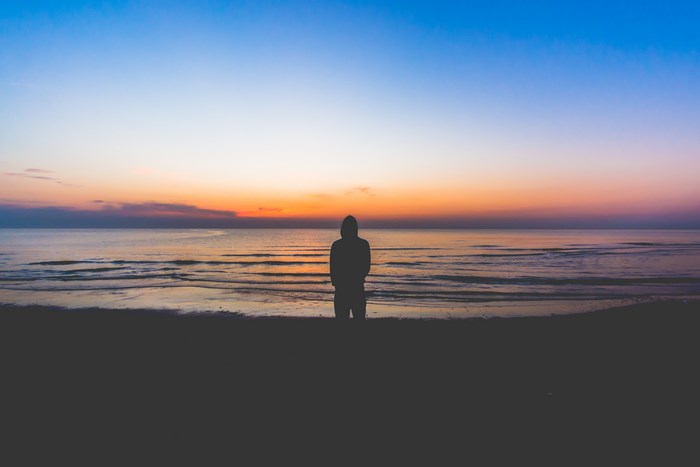 Silhouette Standing by Calm Ocean at Sunset