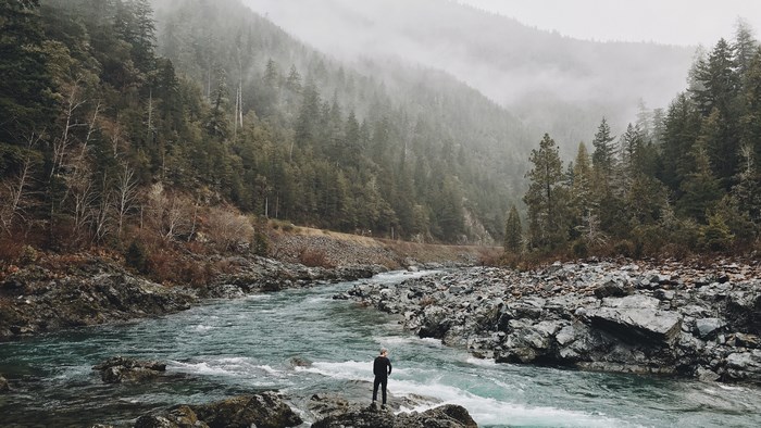 Man standing by a rocky river in a foggy forest