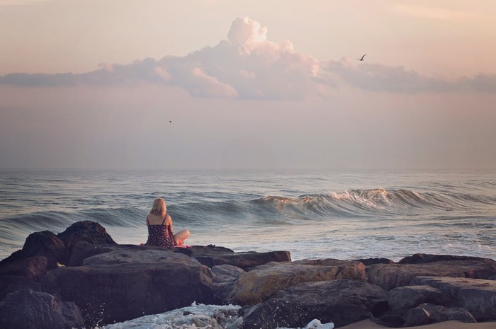 Woman sitting on rocks by the ocean at sunrise
