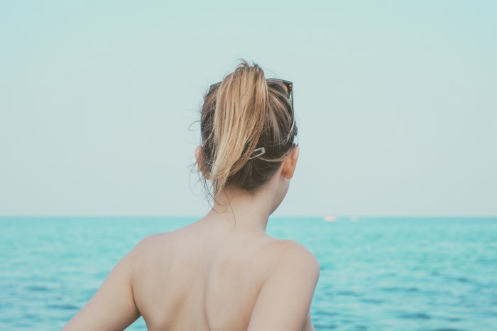 Woman with blonde ponytail looking at the ocean in Greece