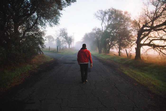 Man in red jacket walks on foggy road