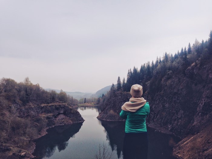 Woman in green jacket looking at a lake and forest