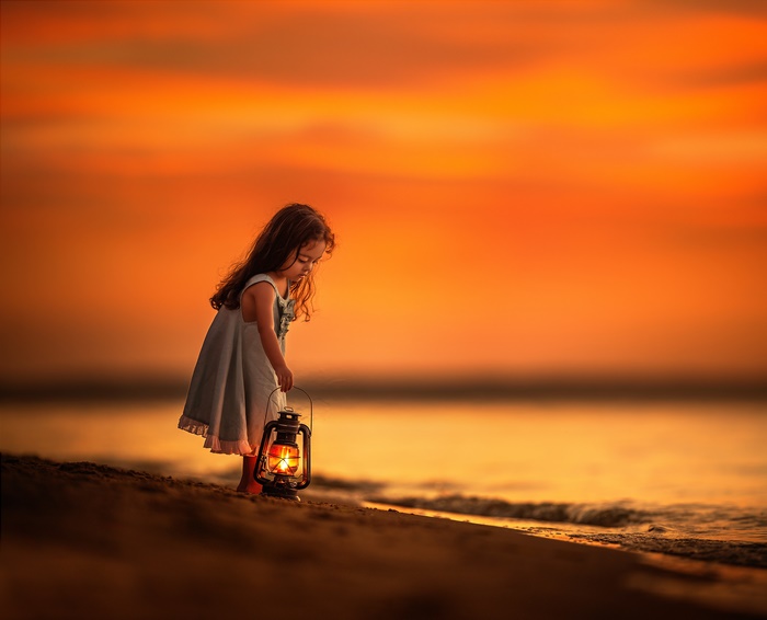 Girl holding a lantern on the beach at sunset