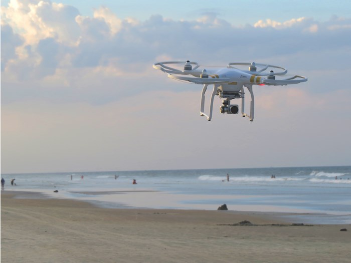 DJI Phantom drone flying over a beach with ocean waves