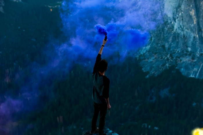 Person holding a blue smoke bomb on a mountain