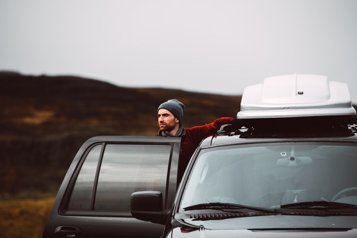 Man in beanie leaning on car with roof box
