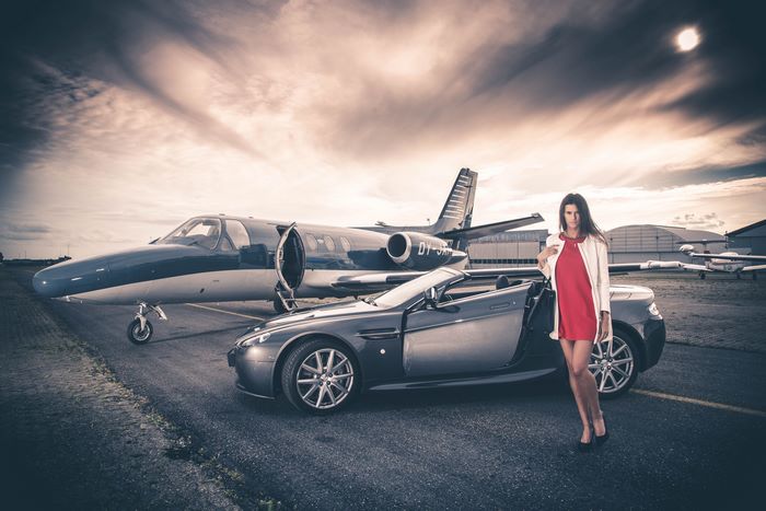 Woman in red dress with Aston Martin and private jet